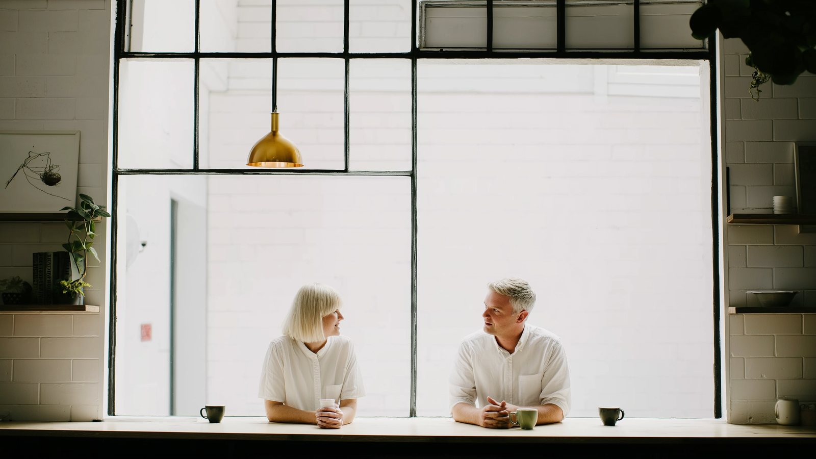 Two colleagues facing each other across a white counter with coffee, in a bright office
