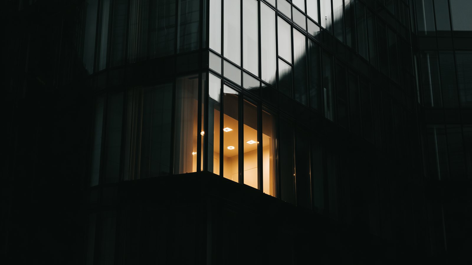 An office facade at night, almost entirely dark, with one floor still lit from inside