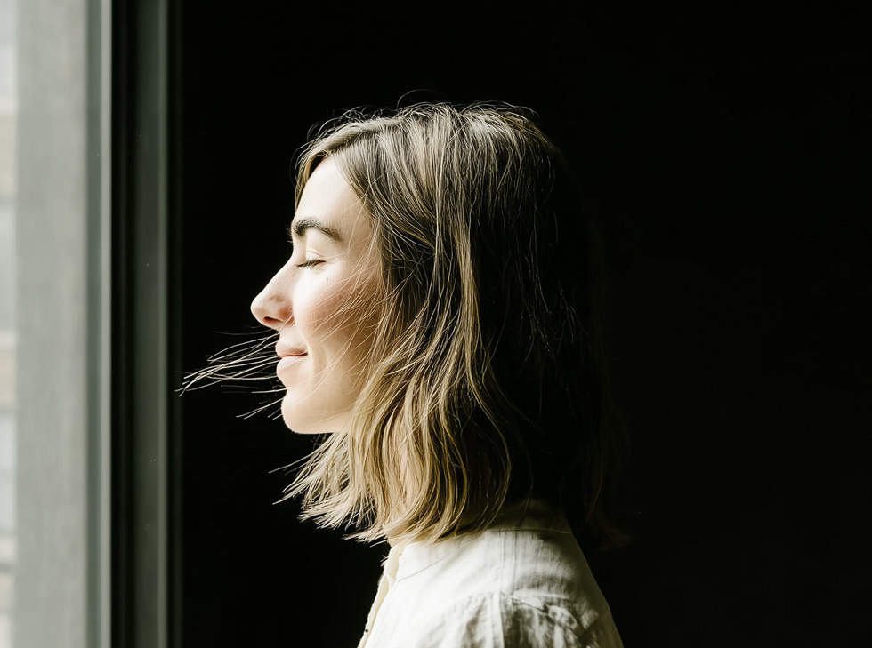 Een vrouw en profil bij een raam, ogen dicht in het licht