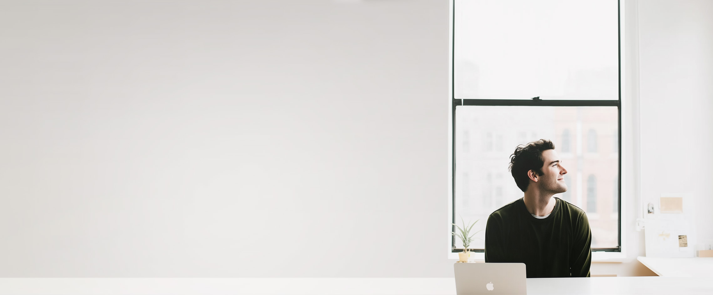 A man at a desk by a tall office window, looking out